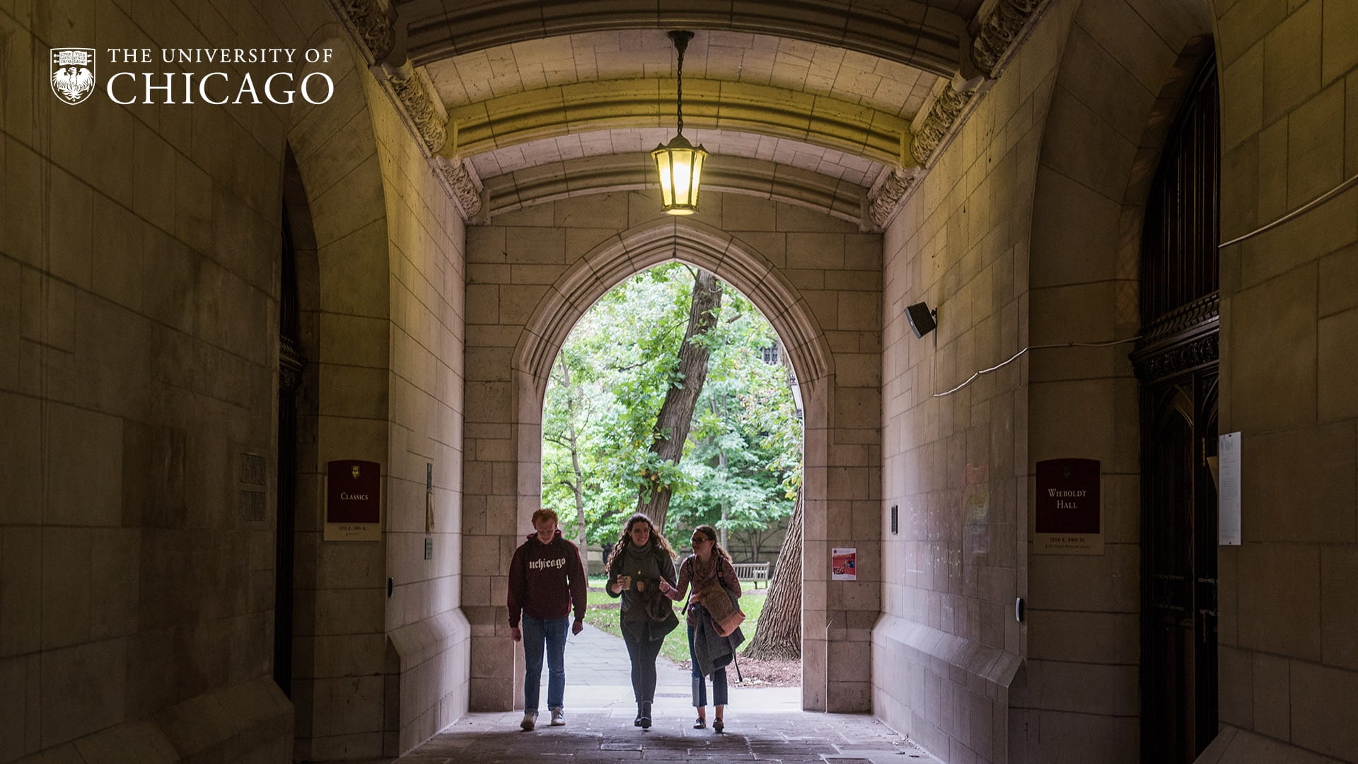 Students walking through a stone archway off a pathway towards the camera
