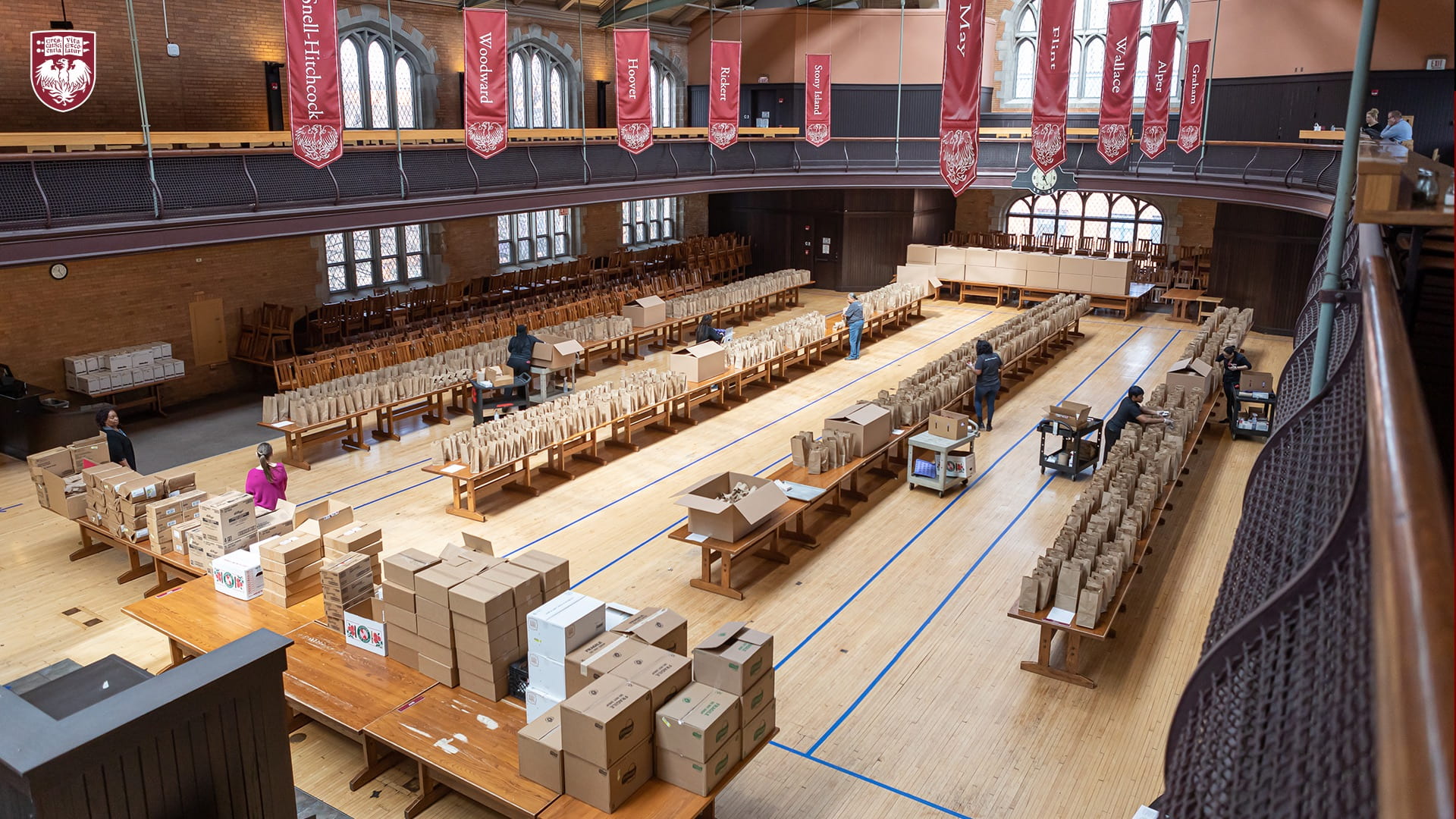 Aerial view of food donation assembly brown paper bags lined up on tables in a gym